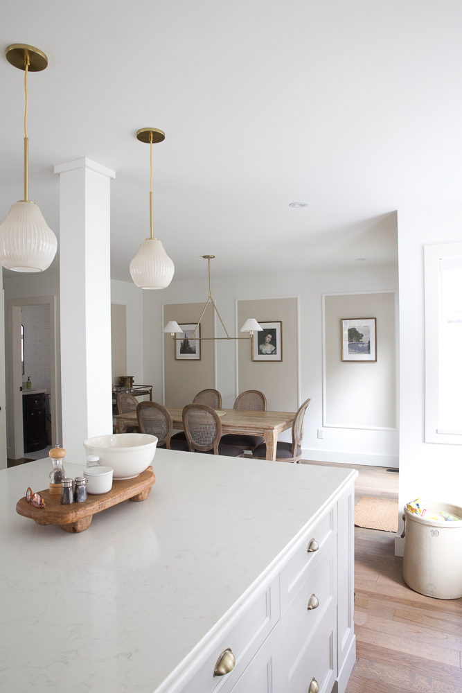New brass or gold light fixtures in white kitchen/neutral dining room.