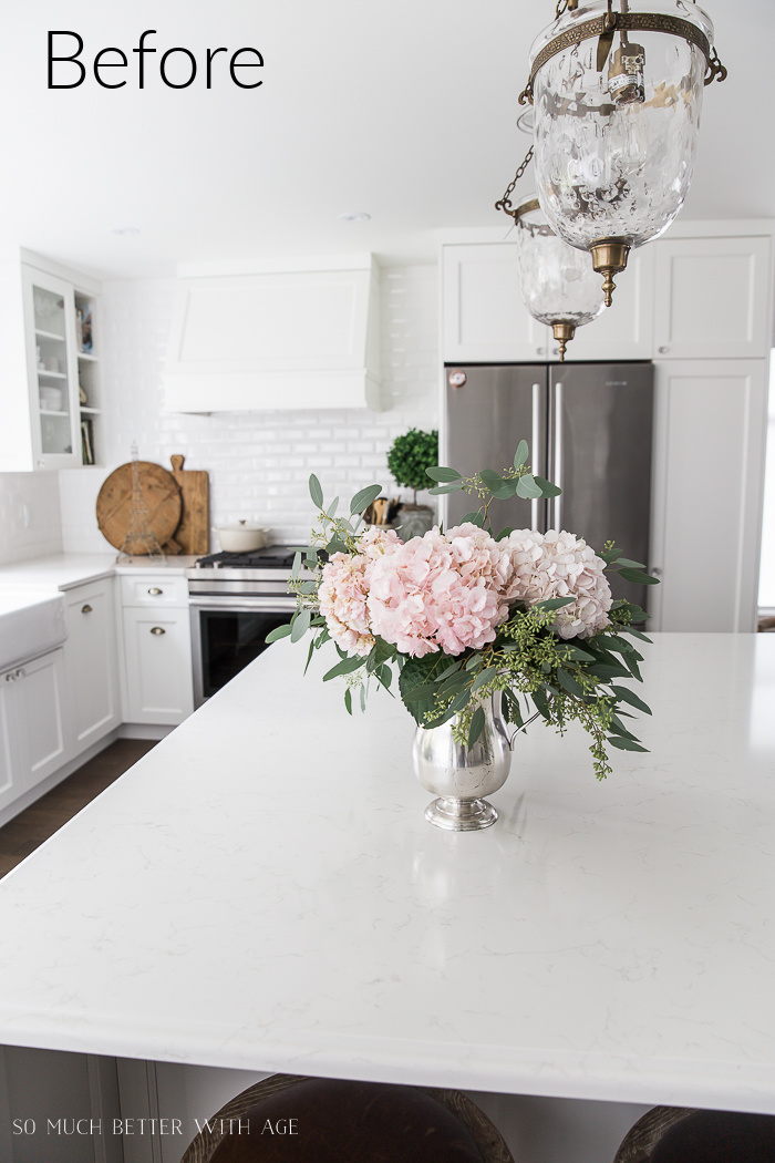 Urn pendant light fixtures hanging above large white kitchen island in all white kitchen.