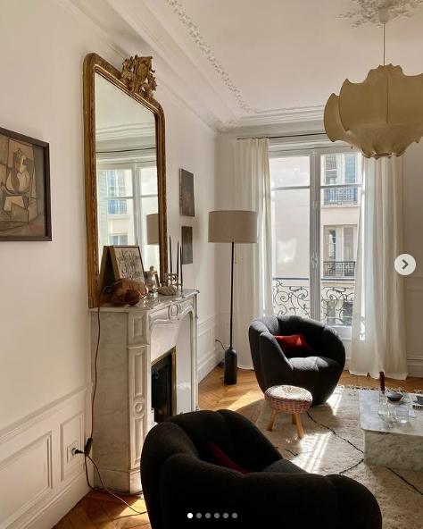French apartment with modern furniture and marble fireplace with gold mirror above it. 