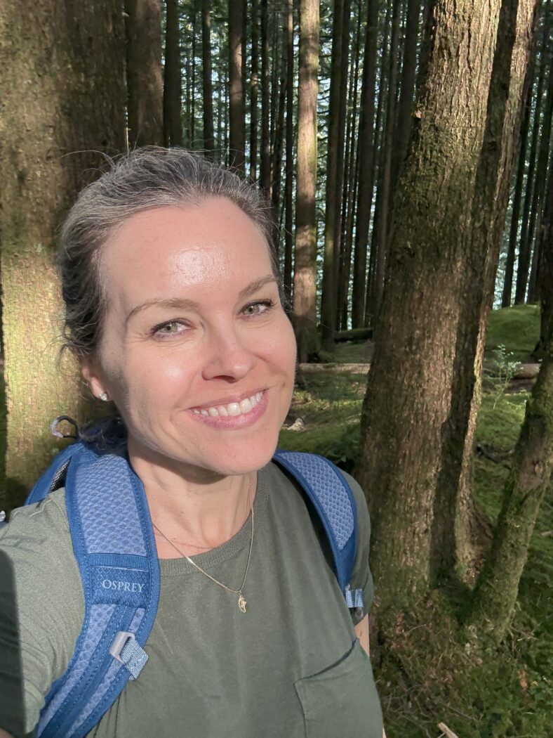 Woman smiling in forest with backpack.