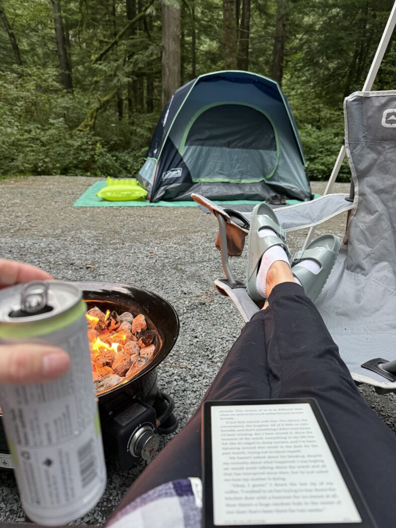 Sitting by camp fire with tent in background.