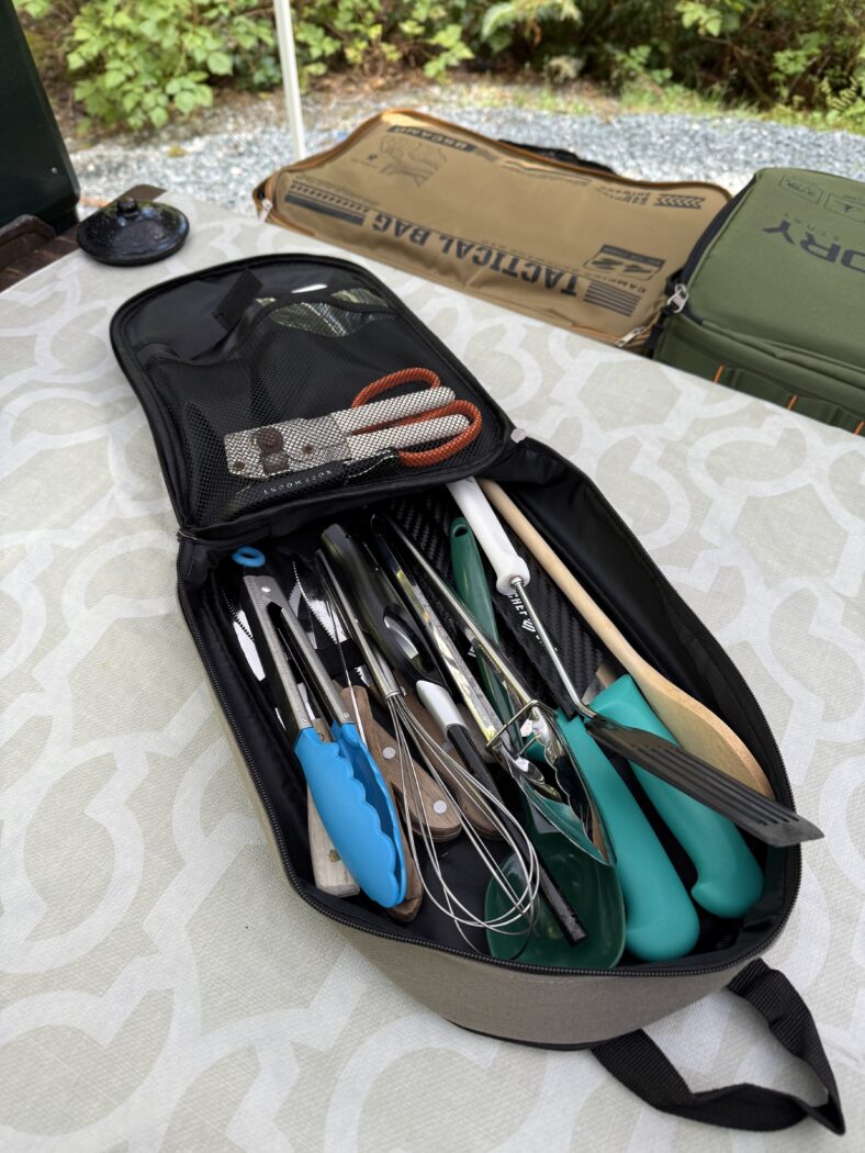 Camping utensil bag with utensils on picnic table.