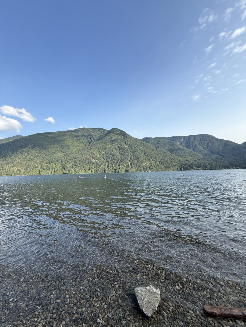 Clear lake with green mountains on sunny day.