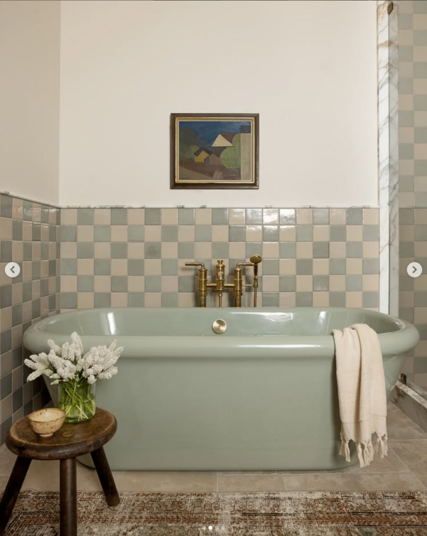 Green free standing tub in bathroom with cream and green tiles. 