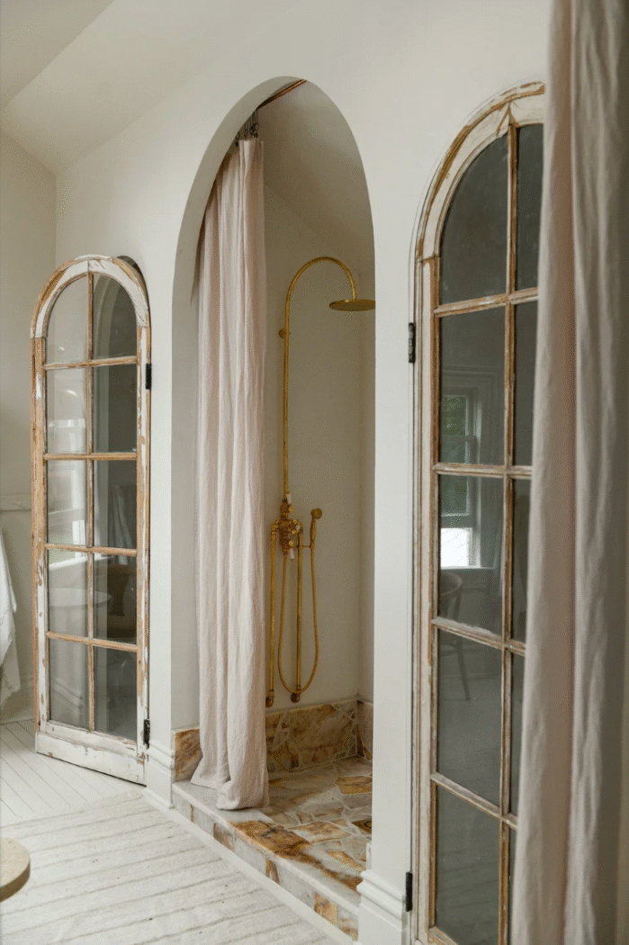 Bathroom with arches and old glass doors and linen shower curtain by Leanne Ford. 