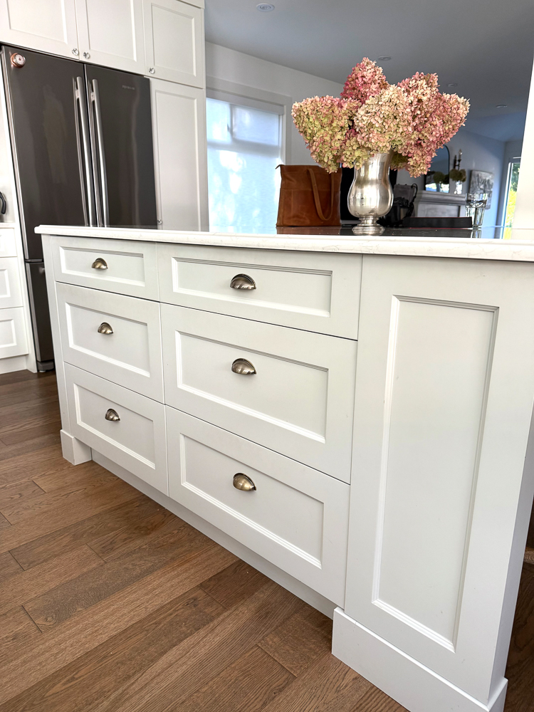 Kitchen island drawers with gold pulls and hydrangeas in silver pitcher on countertop.