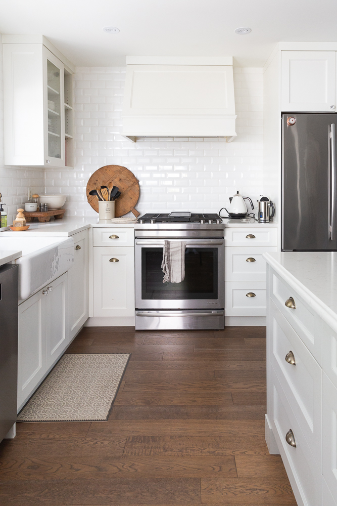 White kitchen with white tile and white countertop and stainless steel appliances.