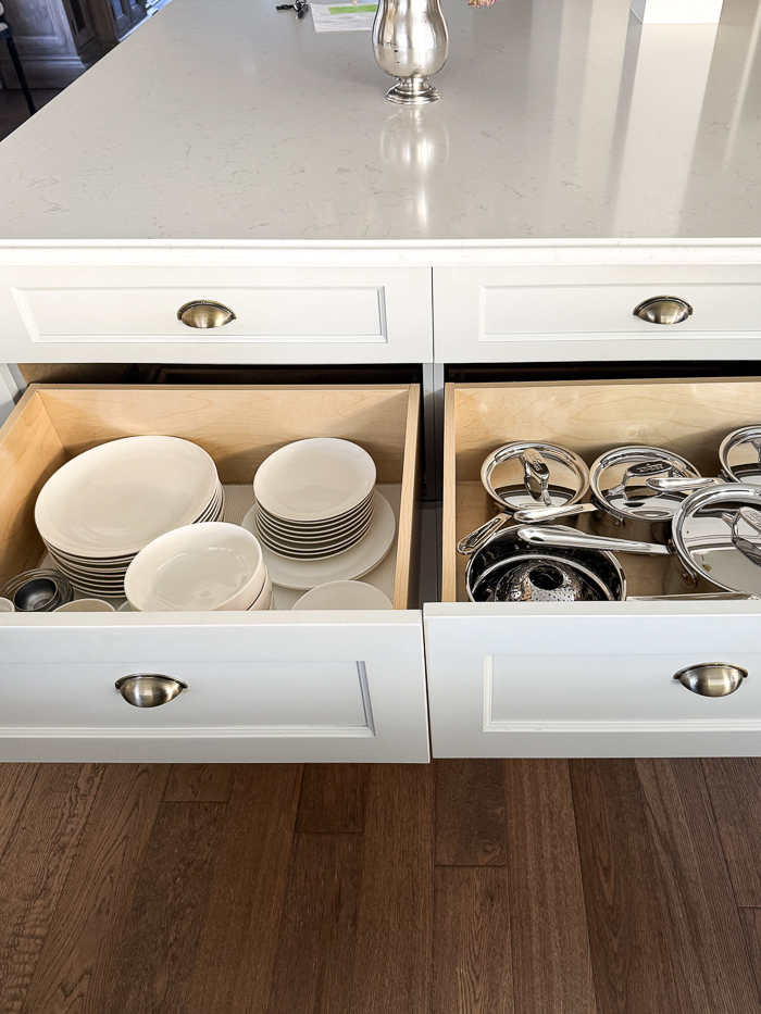 Two drawers of kitchen island pulled out with bowls, plates and pots and pans.