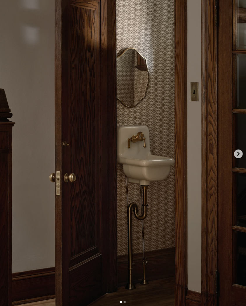 Smallest sink in bathroom with wooden trim and wallpaper behind it.