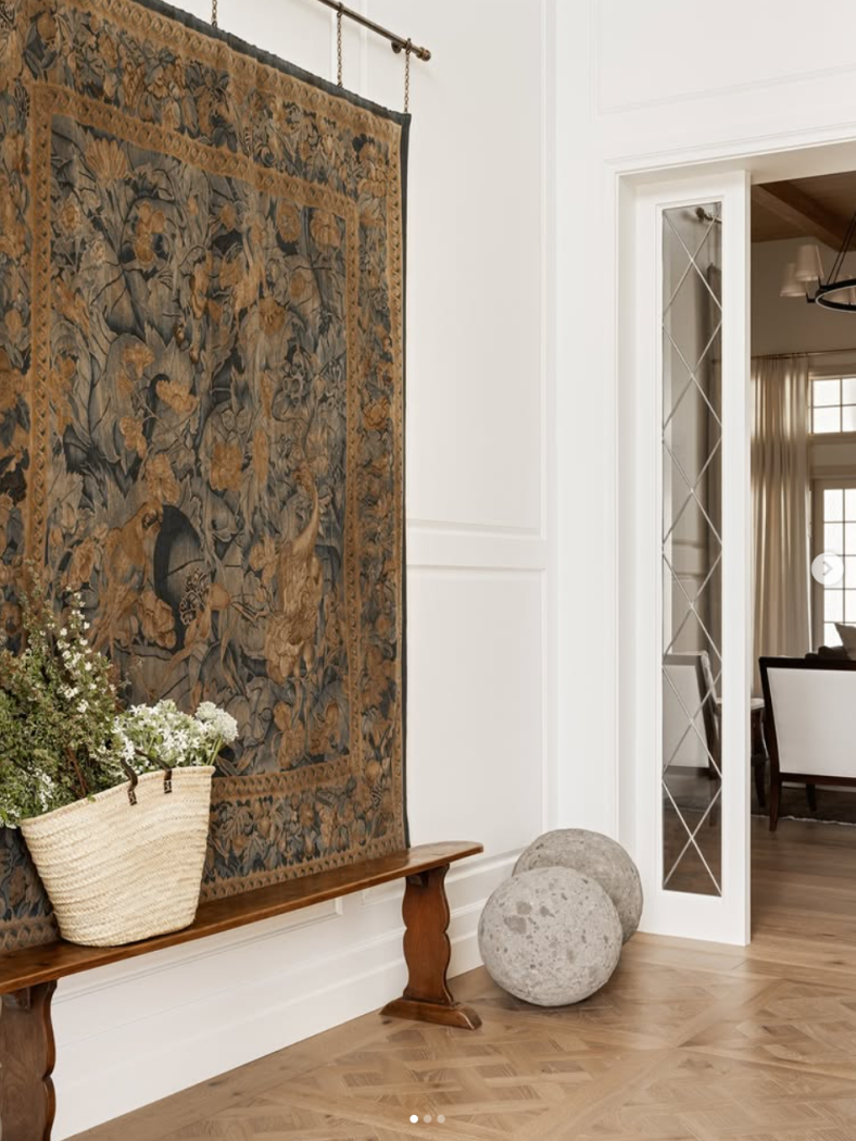 Large tapestry hung on wall in entryway with wood bench and French bag with flowers.