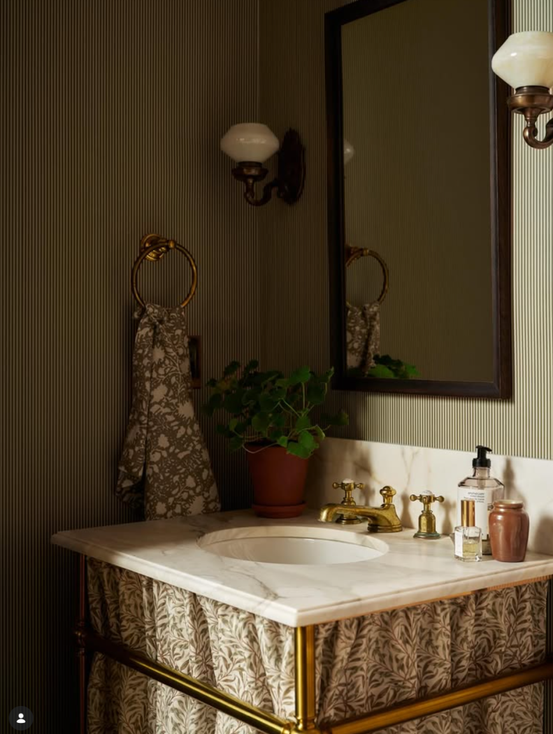Skirted pedestal sink in powder room with marble countertop and green striped wallpaper.